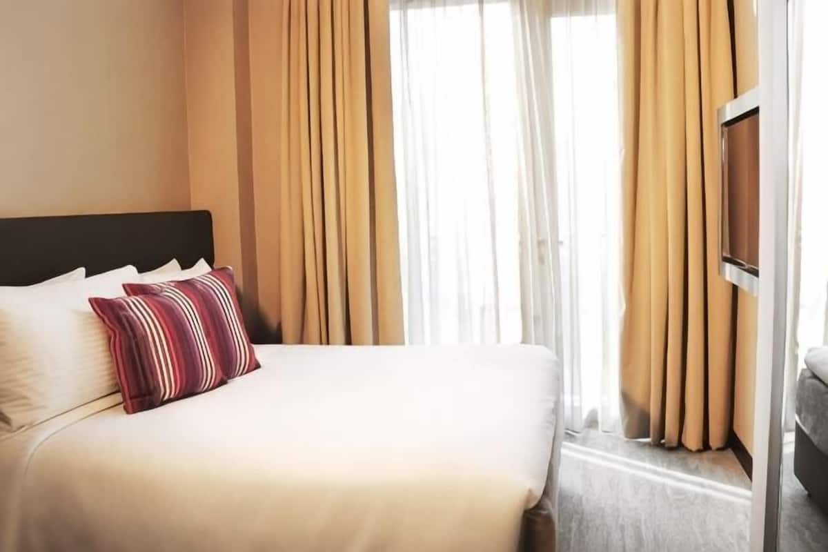 Habitació d'hotel amb llit, cortines i televisió.