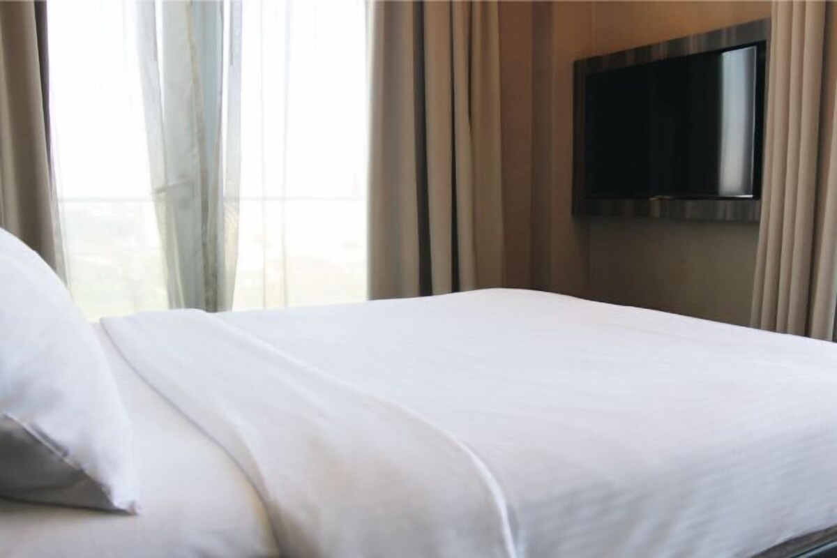 Une chambre d’hôtel avec un lit, des rideaux et un téléviseur fixé au mur.