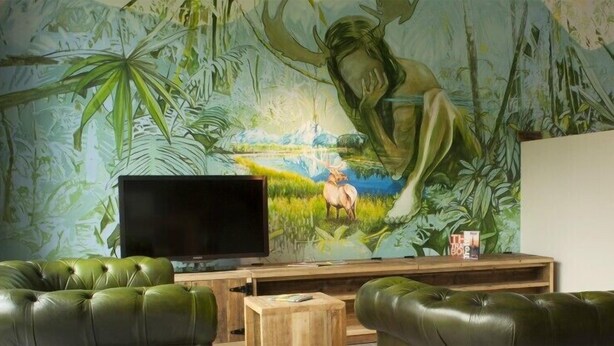 Una sala de estar con un mural grande, un televisor de pantalla plana y sofás de cuero verde.