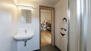 Un baño con lavamanos blanco, un espejo y una pared con una ilustración en blanco y negro de un luchador de sumo.