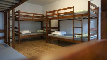 A room with three bunk beds, wooden flooring, and a white wall.