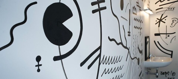 A wall with abstract black and white artwork, a white sink, and a hand sanitizer dispenser. - KaBa Hostel (Ghent)