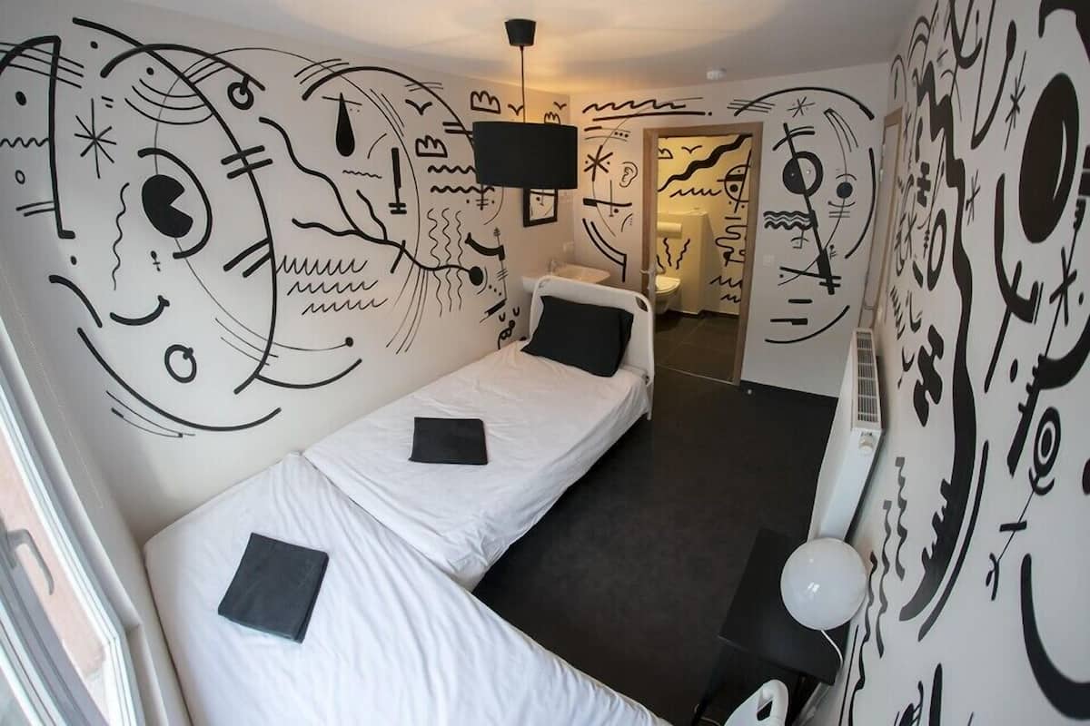 Una habitación con dos camas individuales, un televisor de pantalla plana y paredes decoradas con diseños abstractos en blanco y negro.