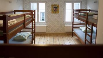 A dormitory room with bunk beds, patterned wallpaper, and a window with a picture frame.