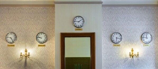 Un vestíbulo de hotel con cuatro relojes de pared, un espejo y dos candelabros.