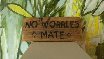 A wooden sign with the text "NO WORRIES MATE" against a backdrop of green foliage.