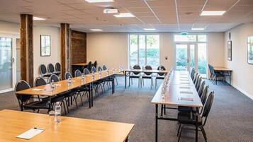 Ett konferensrum med långa bord och stolar, stora fönster och en vägg som har en träpanel som dekorativt inslag.