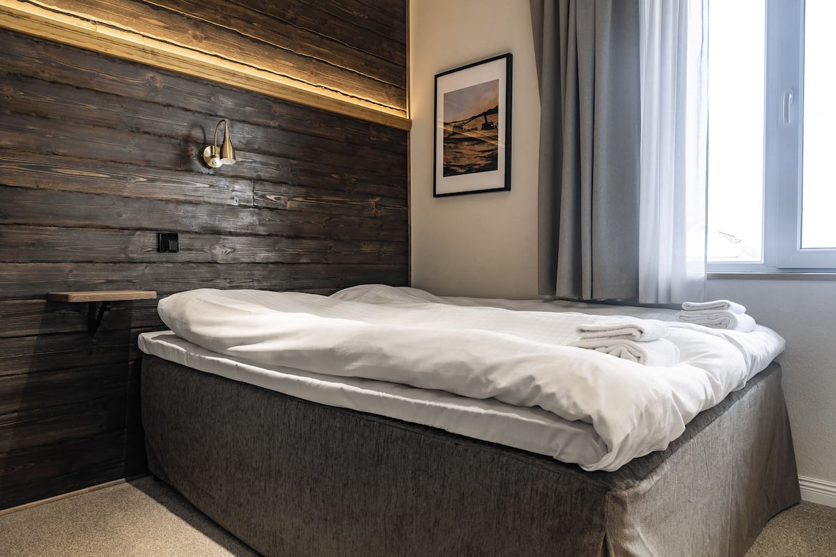 Une chambre à coucher moderne avec une tête de lit en bois, une table de chevet, un tableau encadré et une fenêtre avec des rideaux.
