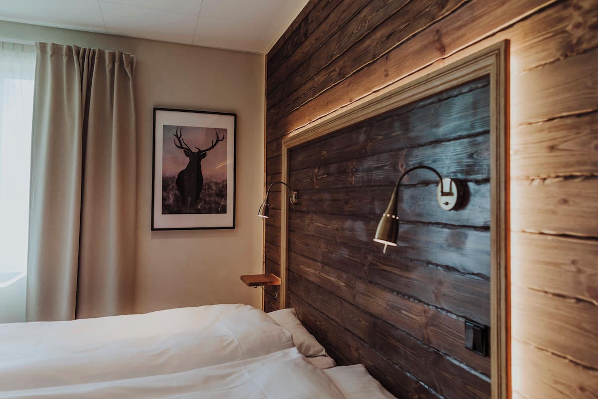 Une chambre à coucher avec une tête de lit en bois, un tableau encadré représentant un cerf, une table de chevet et une lampe.