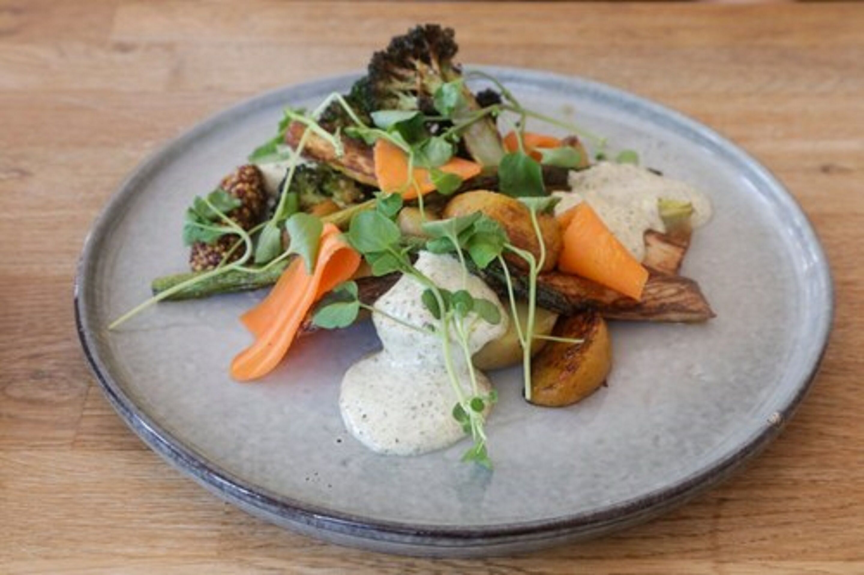 Un plato de vegetales asados con verduras de hoja y salsa cremosa sobre un plato de cerámica.