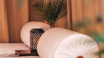 Una cama con ropa de cama blanca, una planta pequeña en maceta y un adorno al lado.