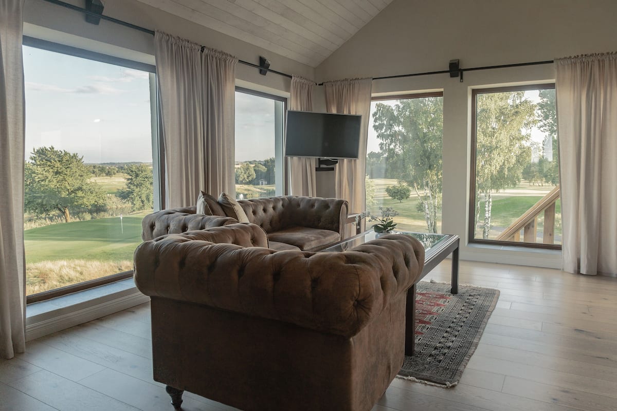 Un salon spacieux doté d’une grande fenêtre donnant sur un terrain de golf, d’un confortable canapé marron, d’un téléviseur à écran plat et d’un plancher en bois.