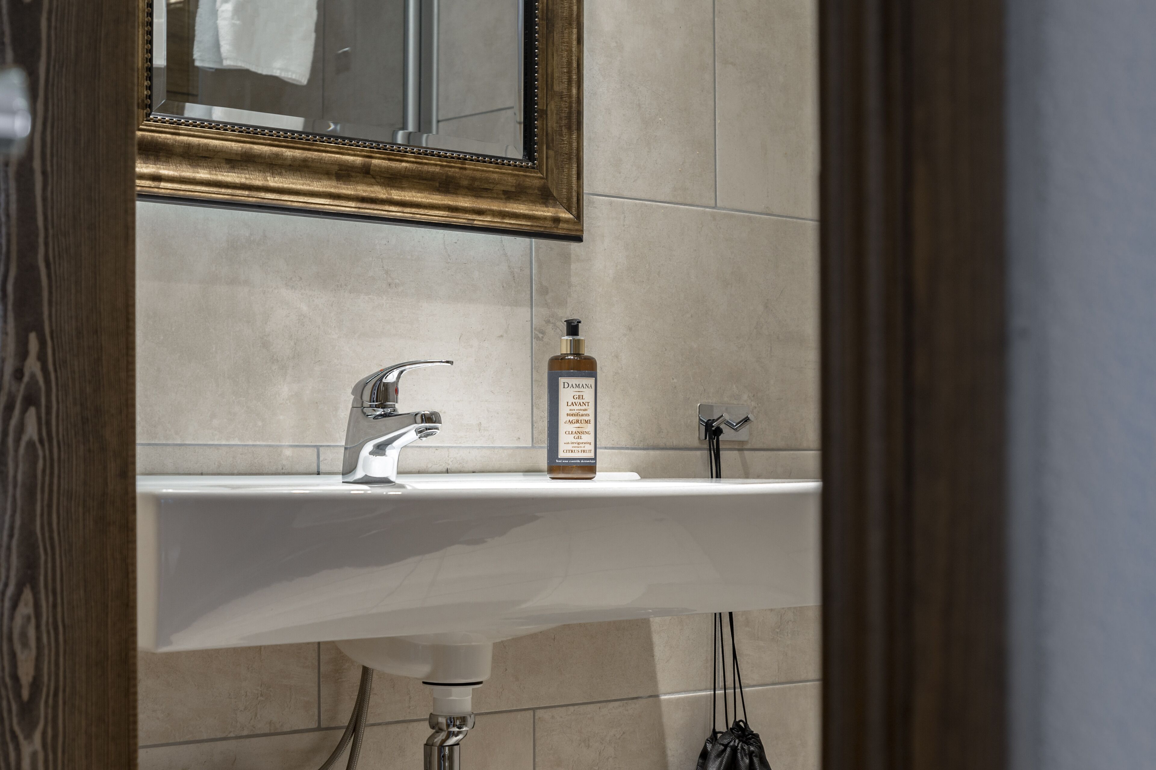 A bathroom with a white sink, a gold-framed mirror, and a bottle of lotion.