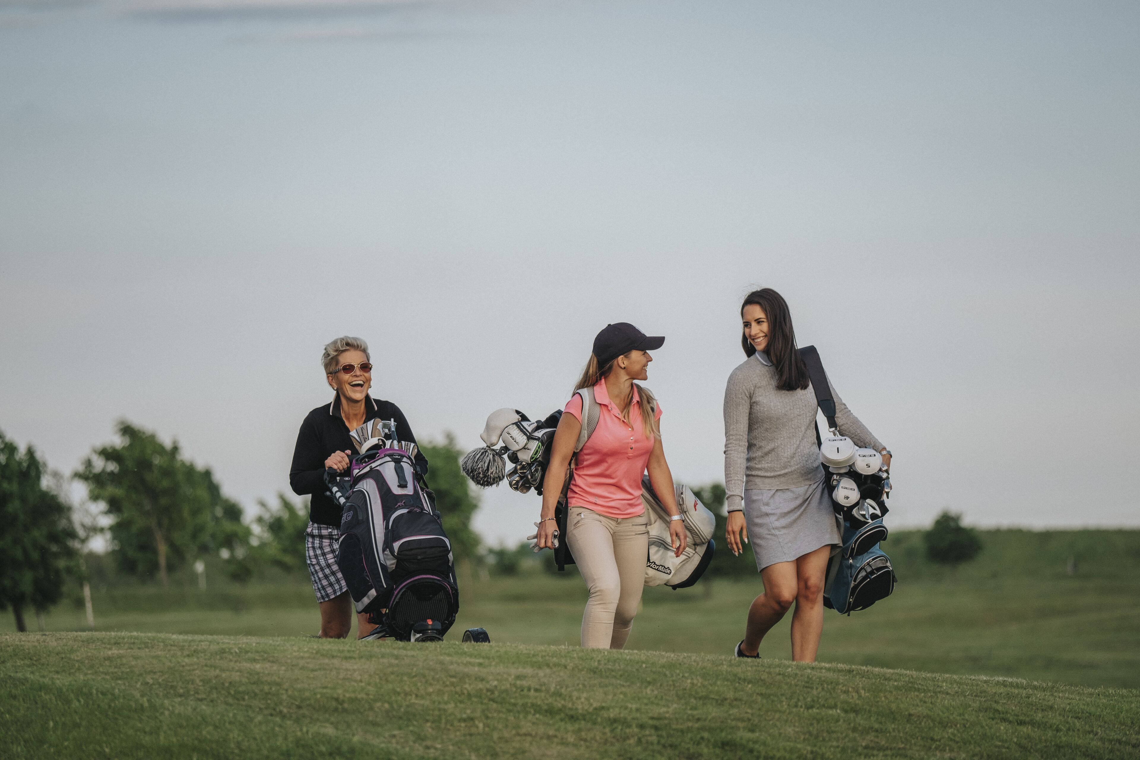 Tres personas caminando sobre un campo de césped, cada una cargando un bolso de golf.