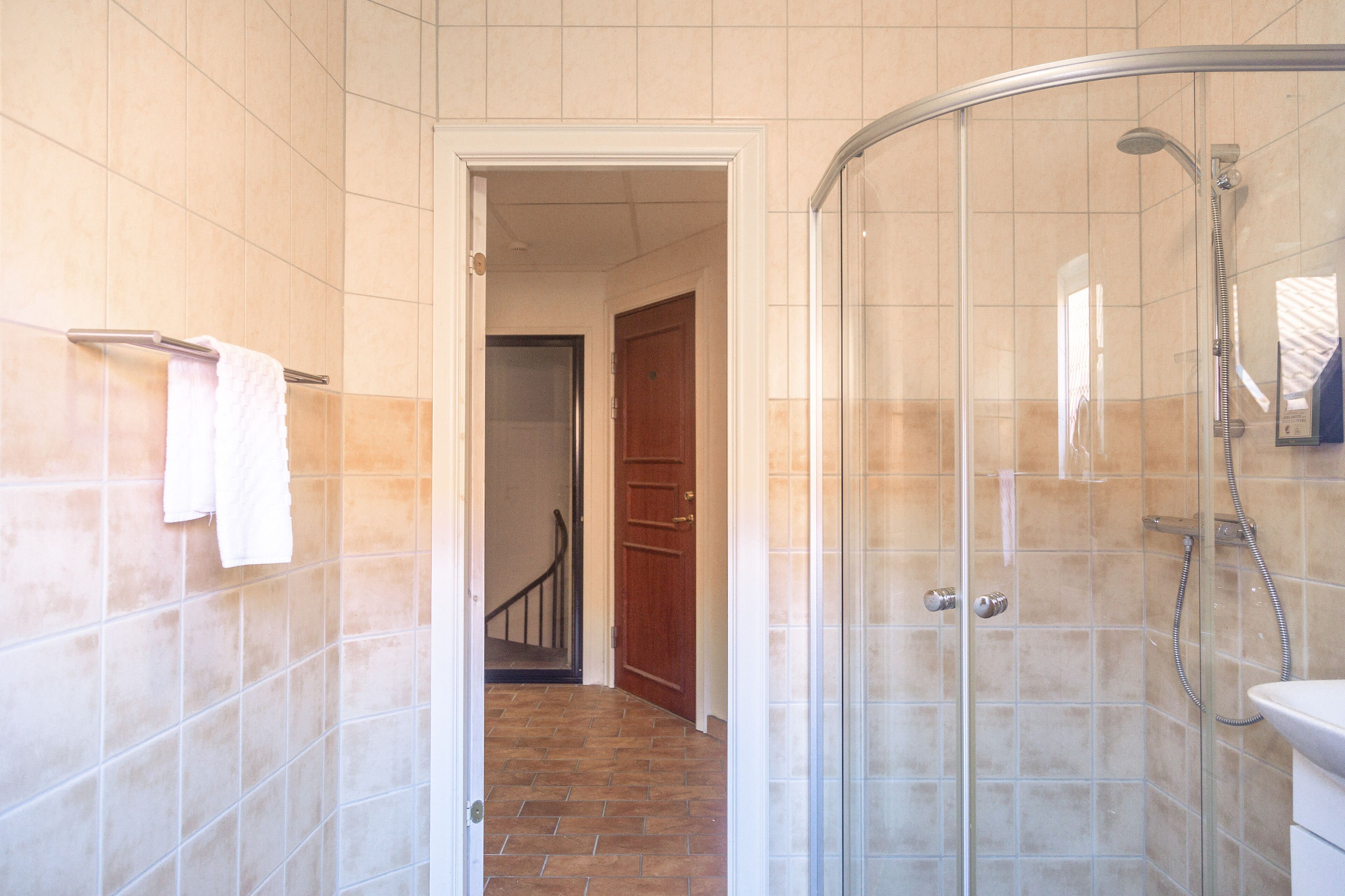 Een badkamer met een douchecabine van glas, een zichtbare deur naar een andere kamer en een betegelde vloer.