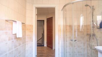 Een badkamer met een douchecabine van glas, een zichtbare deur naar een andere kamer en een betegelde vloer.