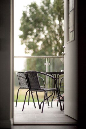 A balcony with two chairs and a table, overlooking a green area with trees. - Lydinge Resort (Hyllinge)
