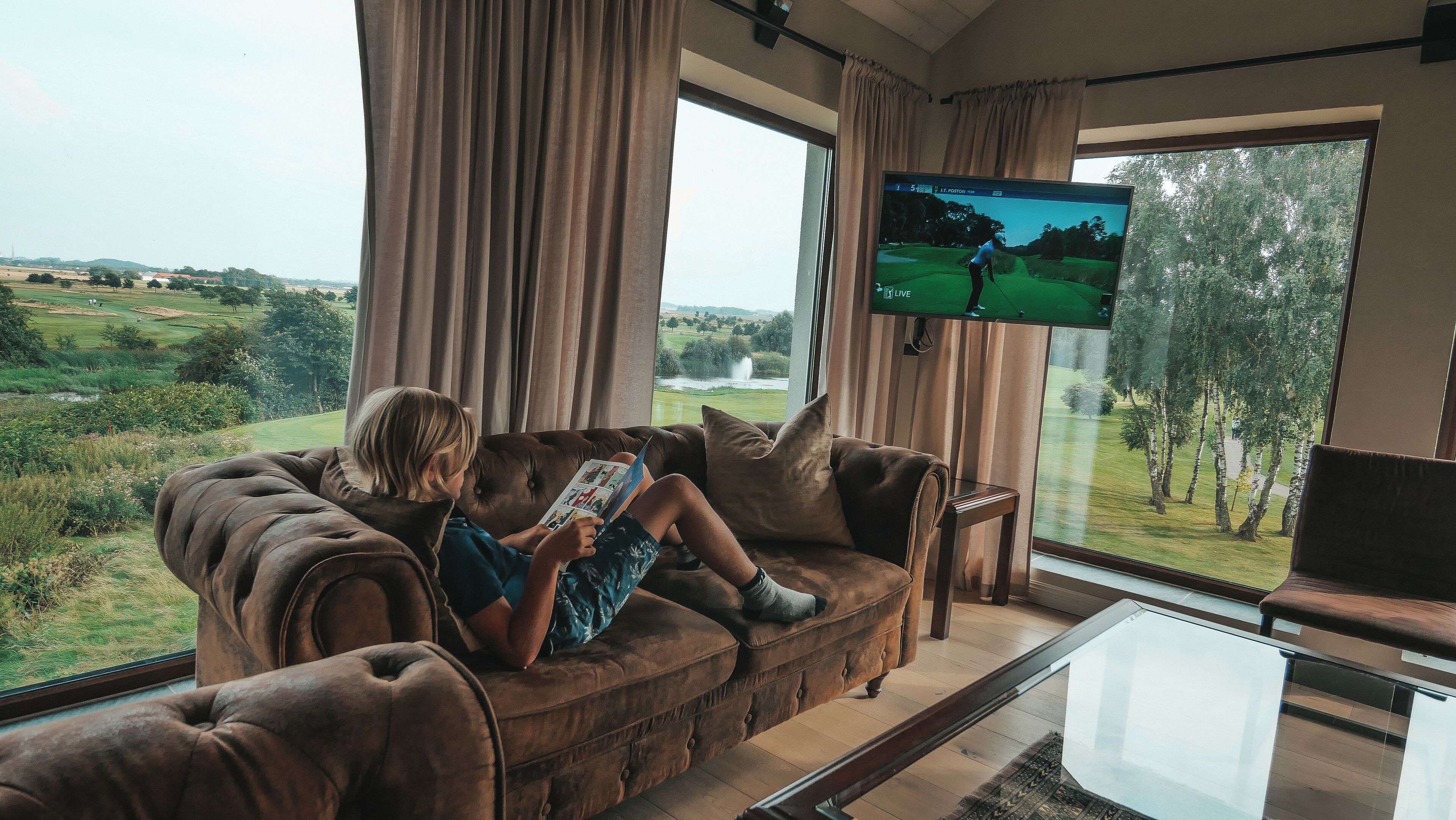 En person sitter i en lädersoffa med utsikt över en golfbana genom stora fönster.