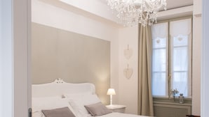 A bedroom with a large bed, a chandelier, a nightstand, and a window with curtains. - Al San Lorenzo (Bergamo)