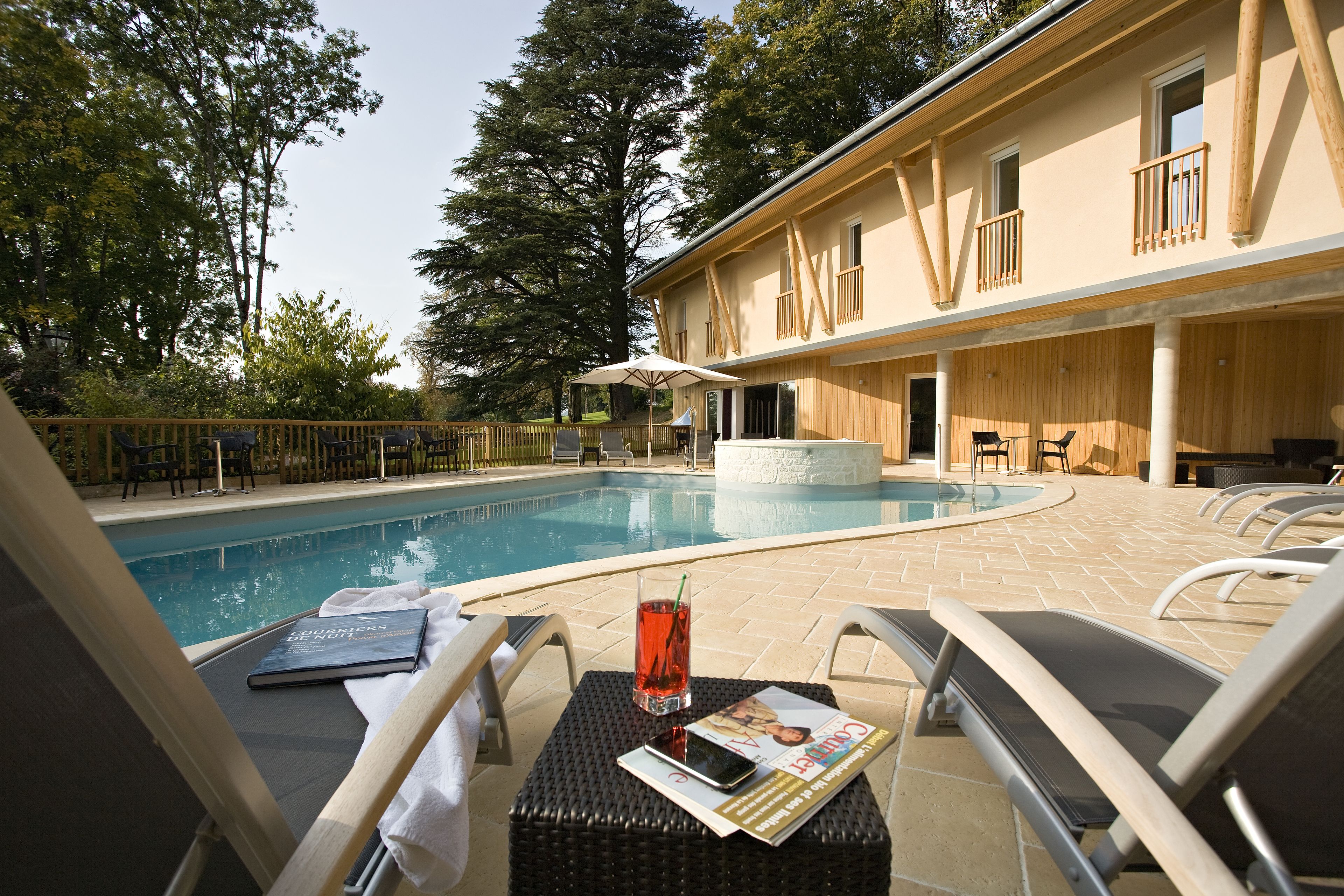 A poolside area with lounge chairs, a table with a magazine and a drink, and a building with wooden balconies.