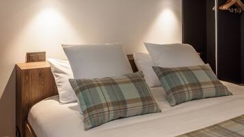 A modern bedroom with a wooden headboard, a large bed with plaid bedding, a nightstand with a lamp, and a wardrobe with hanging clothes.