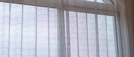 Una habitación con cortinas translúcidas, una lámpara de fibra y un ventanal grande.