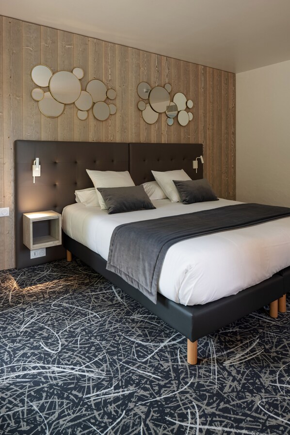 A modern bedroom with a tufted headboard, a bed with white and dark gray bedding, a bedside table, and a wall-mounted mirror. - Logis Hôtel Restaurant Spa Parenthèse (Chille)