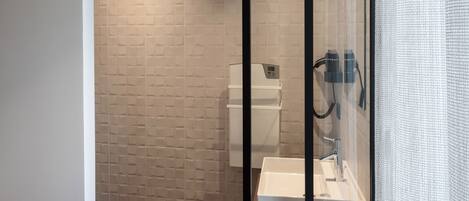 A modern bathroom with a glass shower enclosure, a white sink, and a towel on the counter.