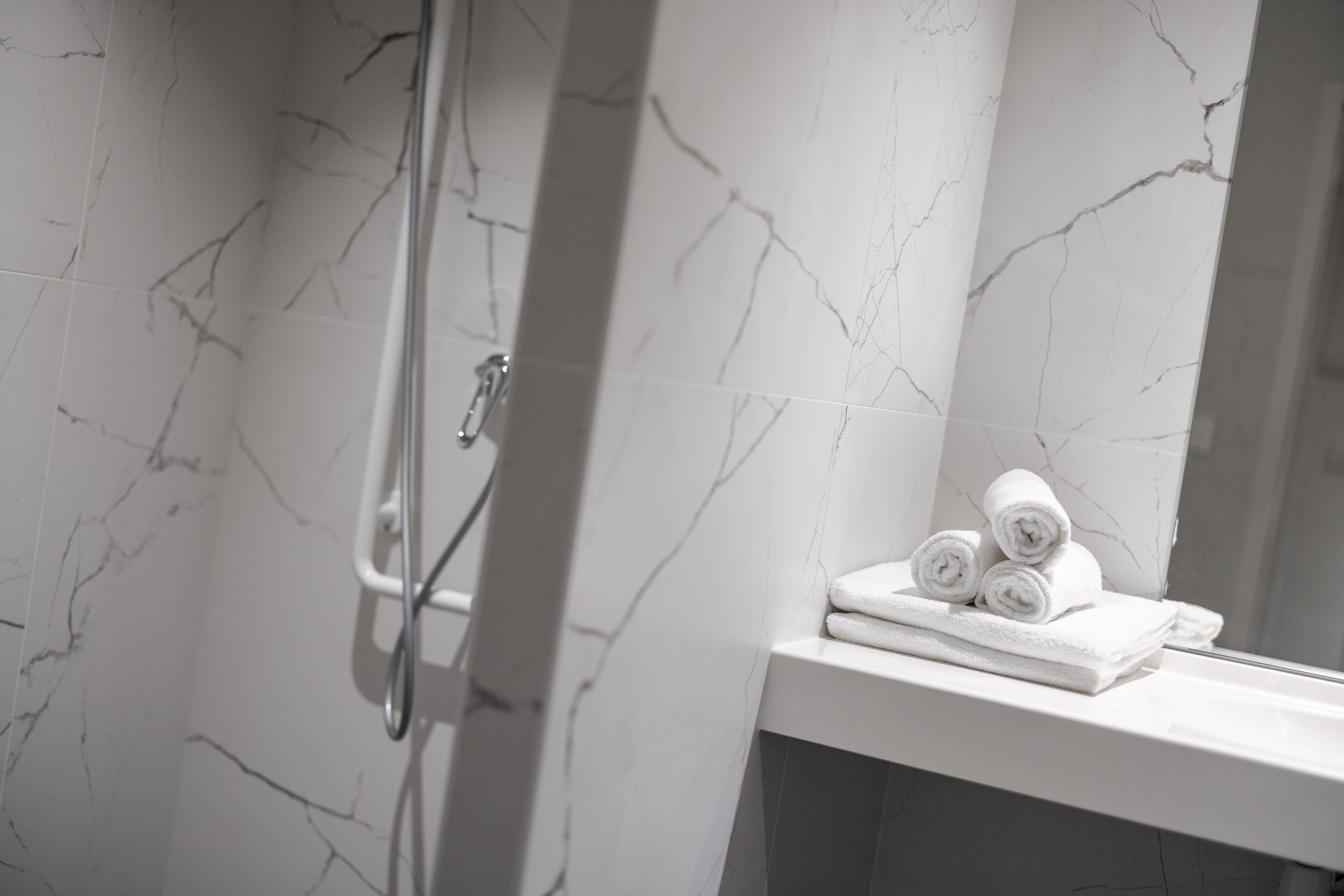 A bathroom with white marble walls and a white sink with towels.