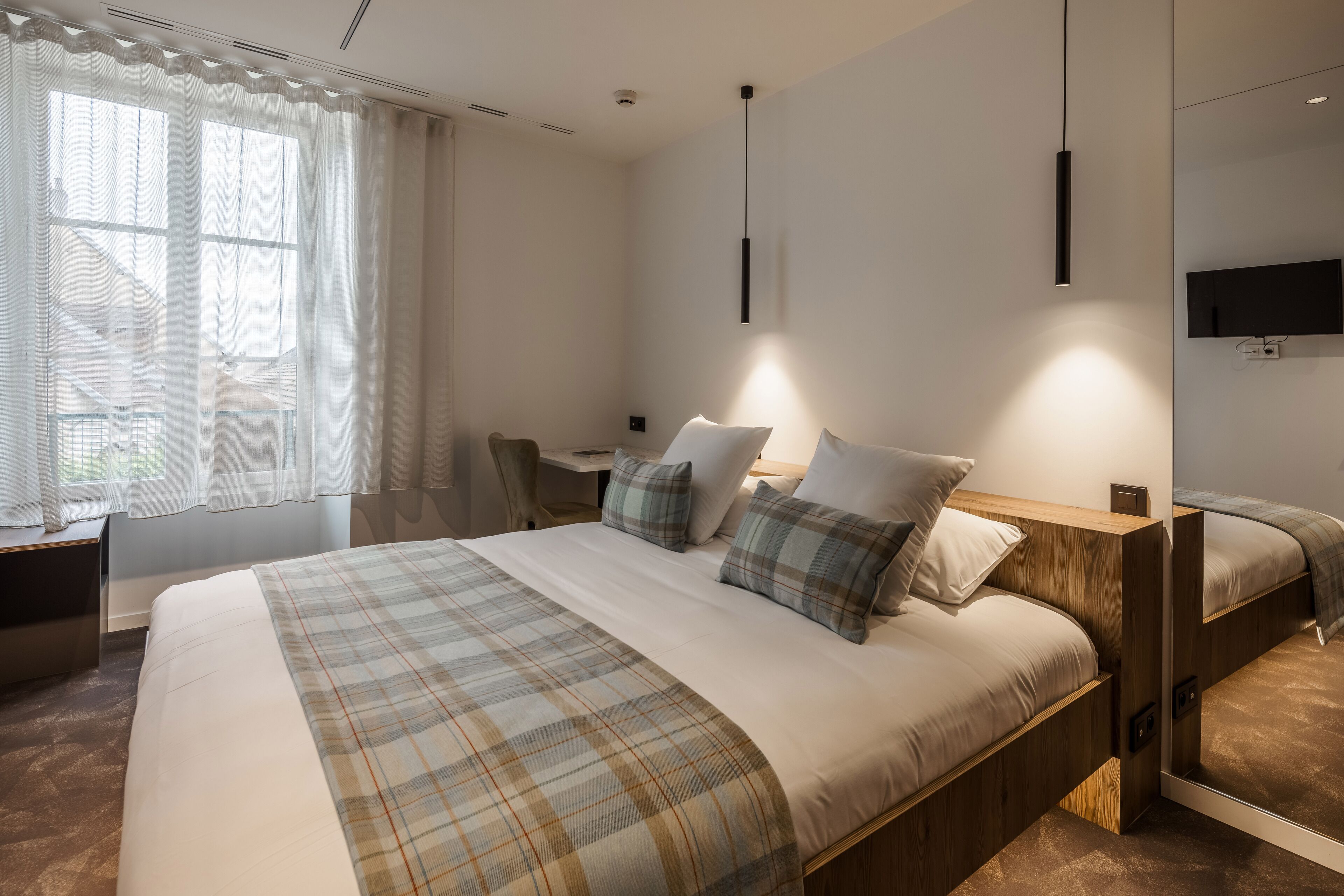 Una habitación de hotel moderna con una cama grande, un escritorio y un televisor en la pared.