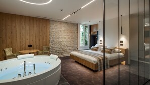 A modern bedroom with a large bathtub, a wooden wall, a stone wall, and a bed with a wooden headboard. - Logis Hôtel Restaurant Spa Parenthèse (Chille)