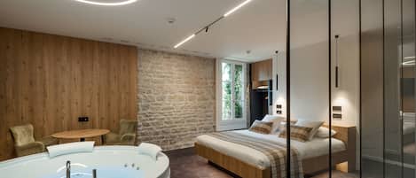 Een moderne slaapkamer met een ruime badkuip, een houten wand, een stenen wand en een bed met een houten hoofdeinde.
