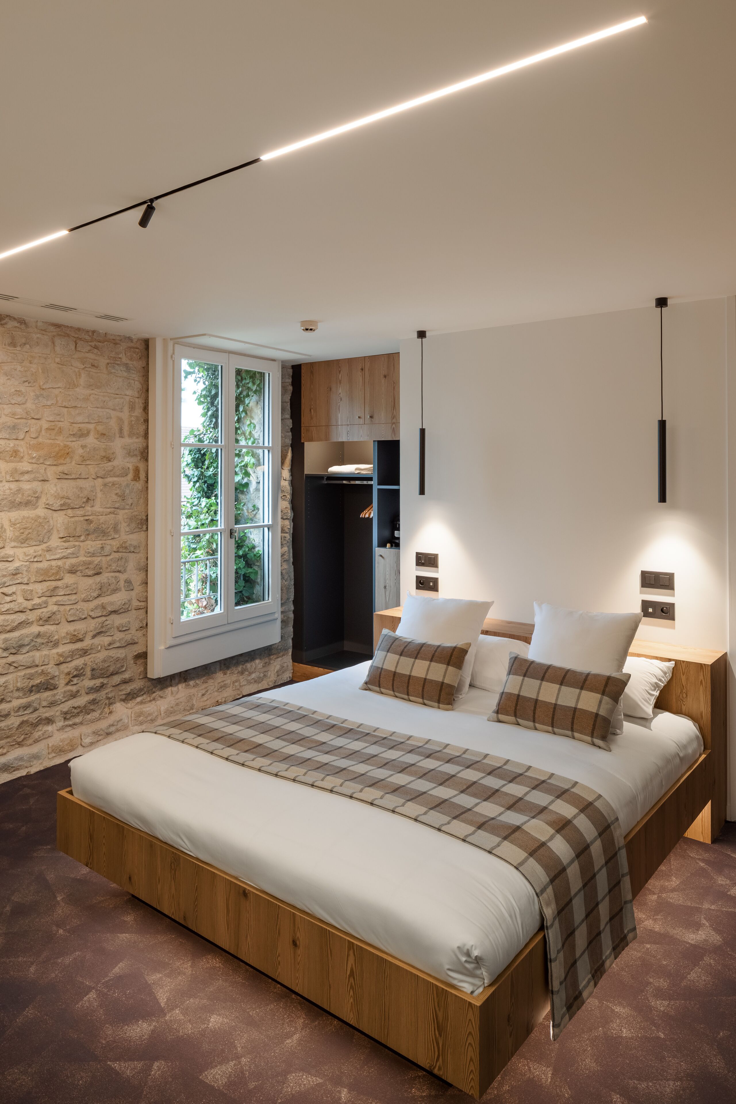 A modern bedroom with a large bed, a stone wall, and a window with a view of greenery.