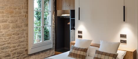 Un dormitorio moderno con una cama grande, pared de piedra y ventana con vista a la vegetación.