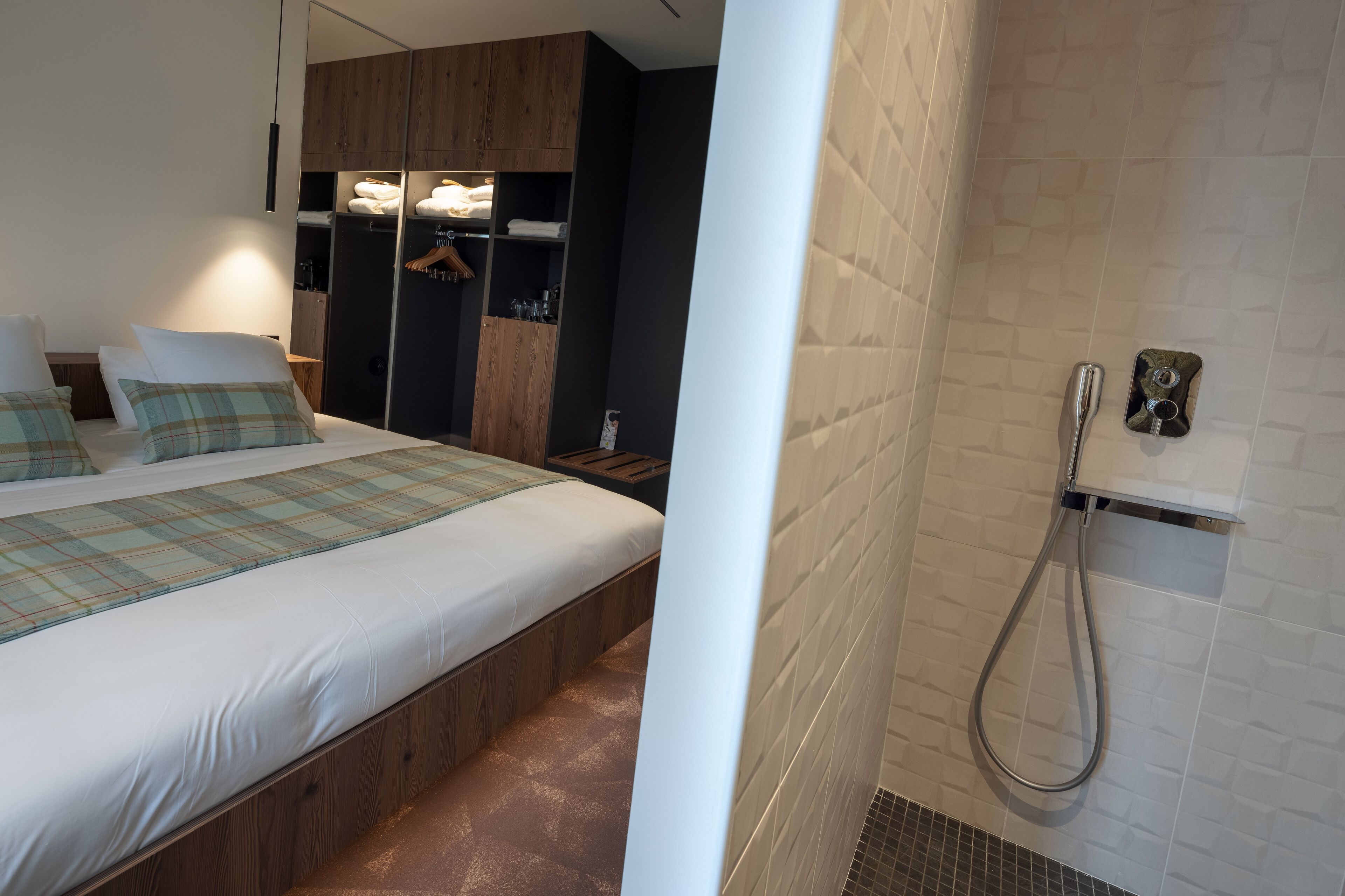A modern hotel room with a large bed, a wooden wardrobe, and a shower area.