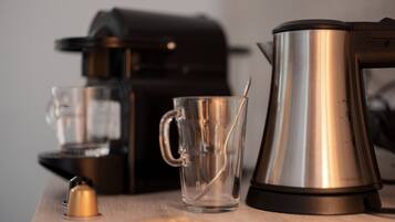 Una cafetera, una taza de vidrio y una cuchara sobre una mesa de madera.