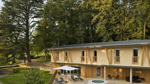 A poolside area with lounge chairs and a hot tub, surrounded by a wooden deck and a large tree. - Logis Hôtel Restaurant Spa Parenthèse (Chille)