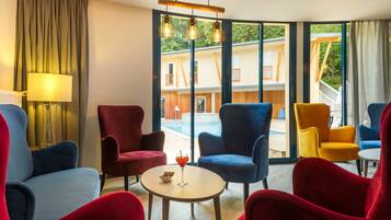 A modern hotel room with a large window, a round table, and colorful chairs.