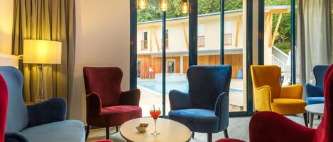 Una habitación de hotel moderna con un ventanal grande, una mesa redonda y sillas coloridas.