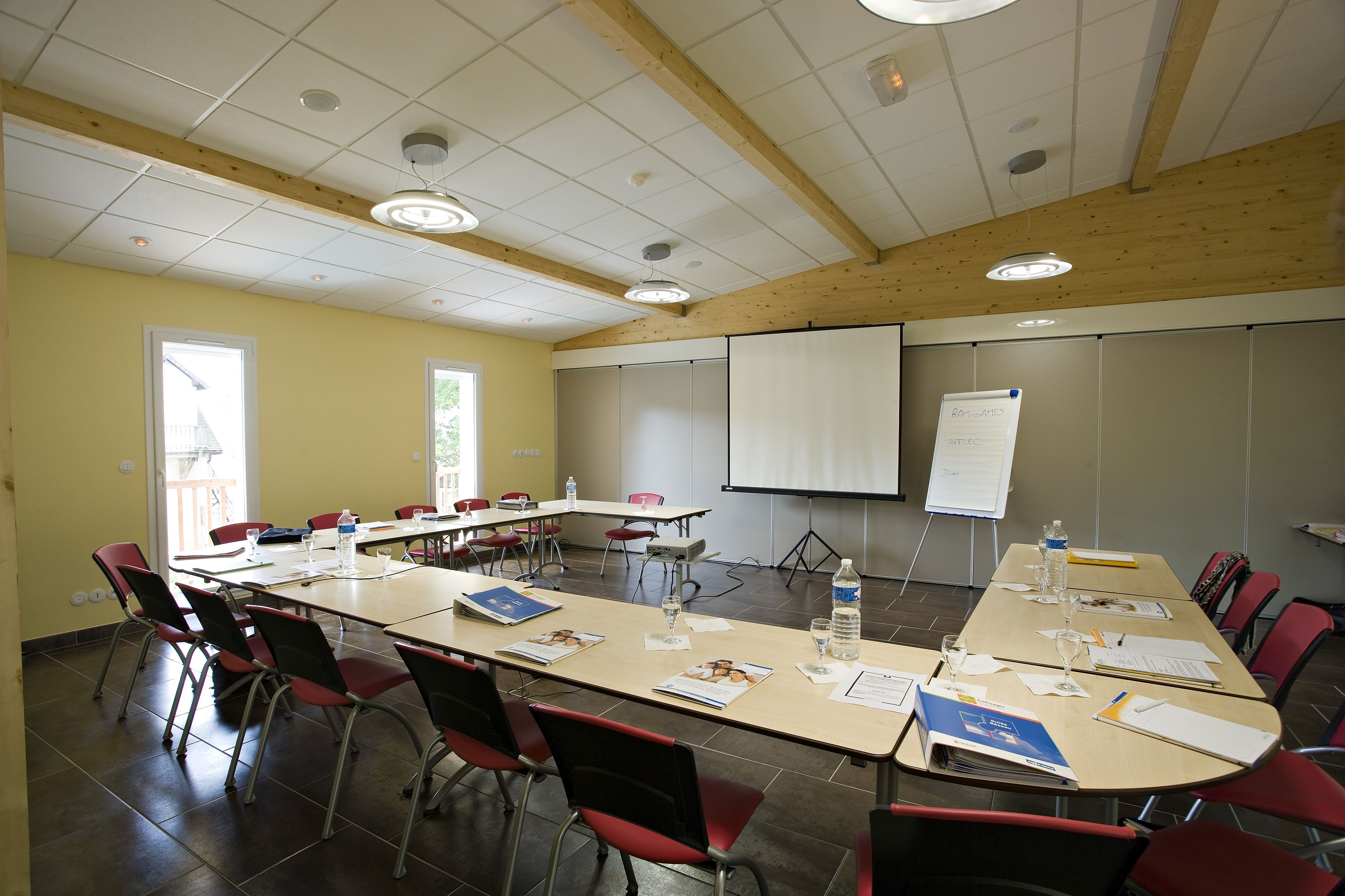 A conference room with a long table, red chairs, and a projector screen.