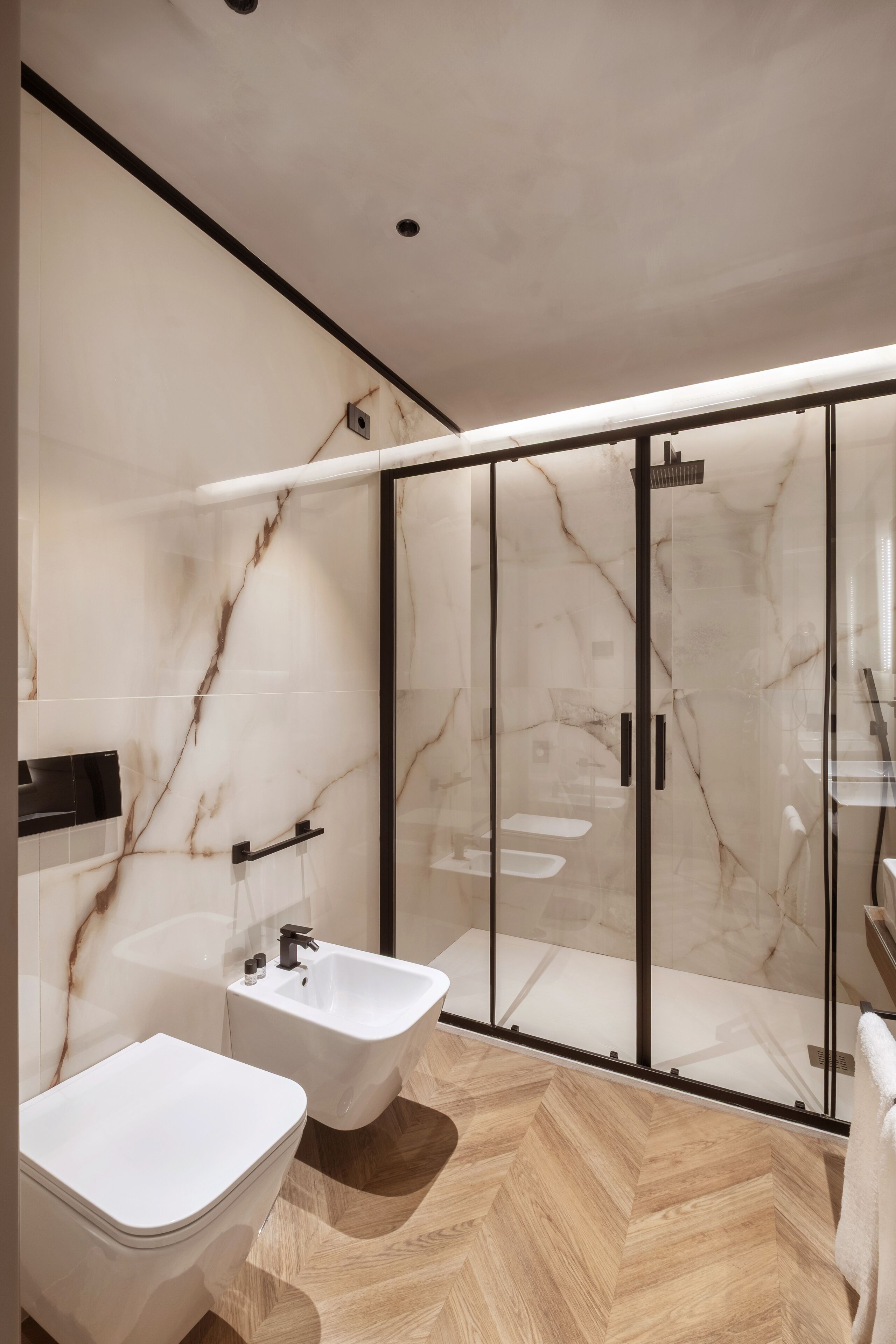 Une salle de bain moderne équipée d’un bidet, d’une douche à parois de verre et d’un mur en marbre.