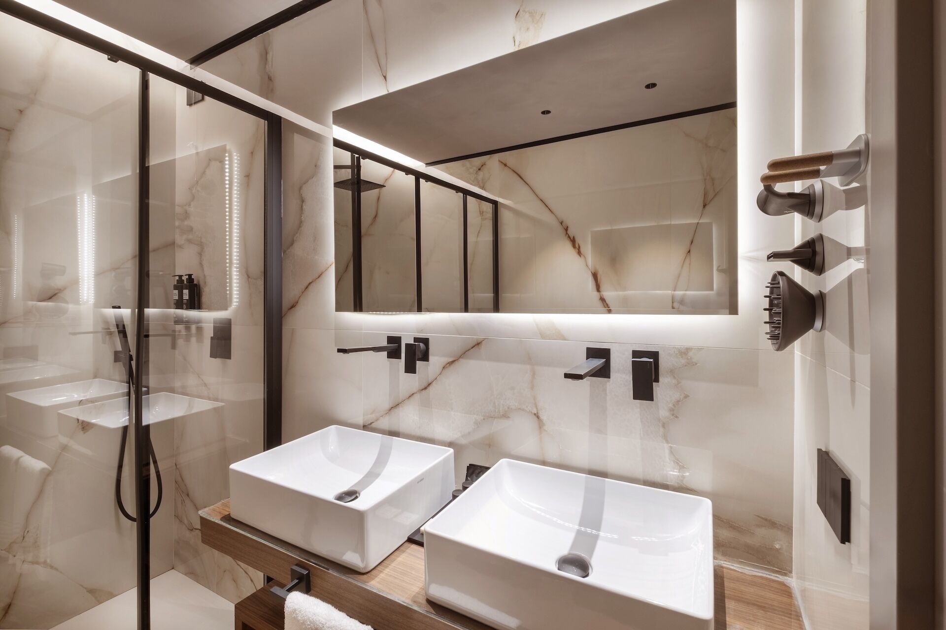 A modern bathroom with two white sinks, a large mirror, and a glass-enclosed shower area.