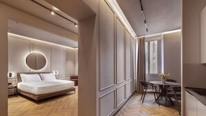 A modern hotel room with a large bed, a round mirror, a dining table with chairs, and a view of the city through the window. - Oriana Homèl Roma (Rome)