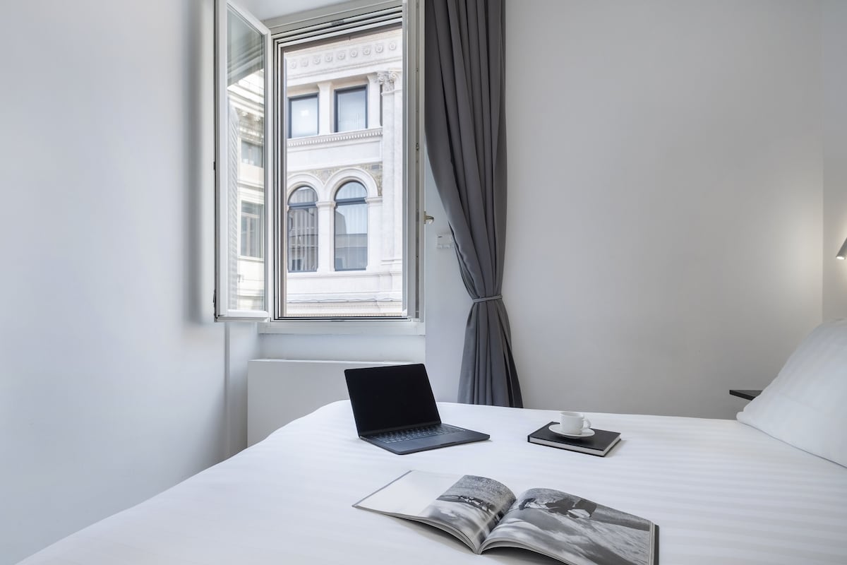 A hotel room with a bed, a laptop, a cup, and an open magazine.