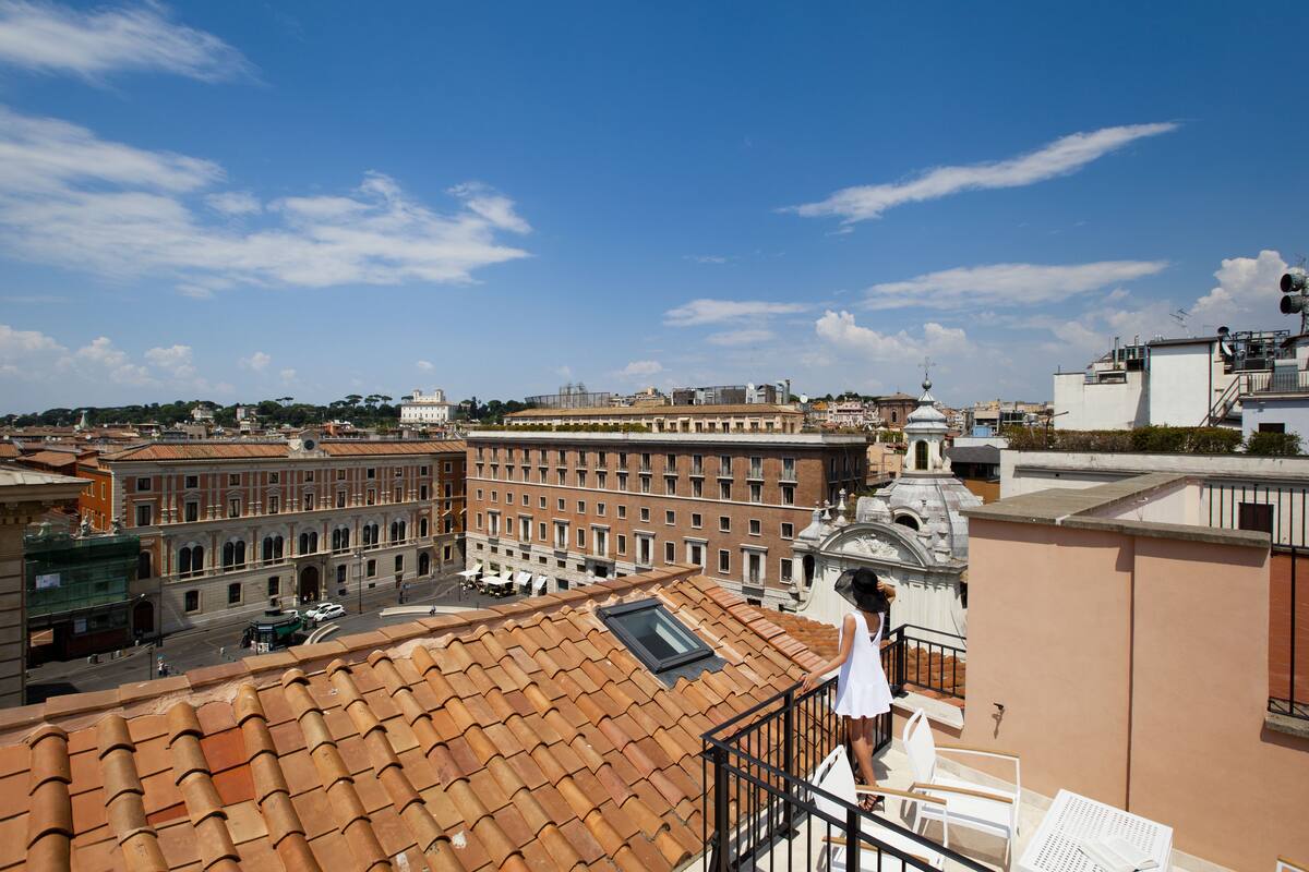 Terraza en la azotea con techo de tejas, barandilla blanca y vista a un edificio histórico con cúpula.