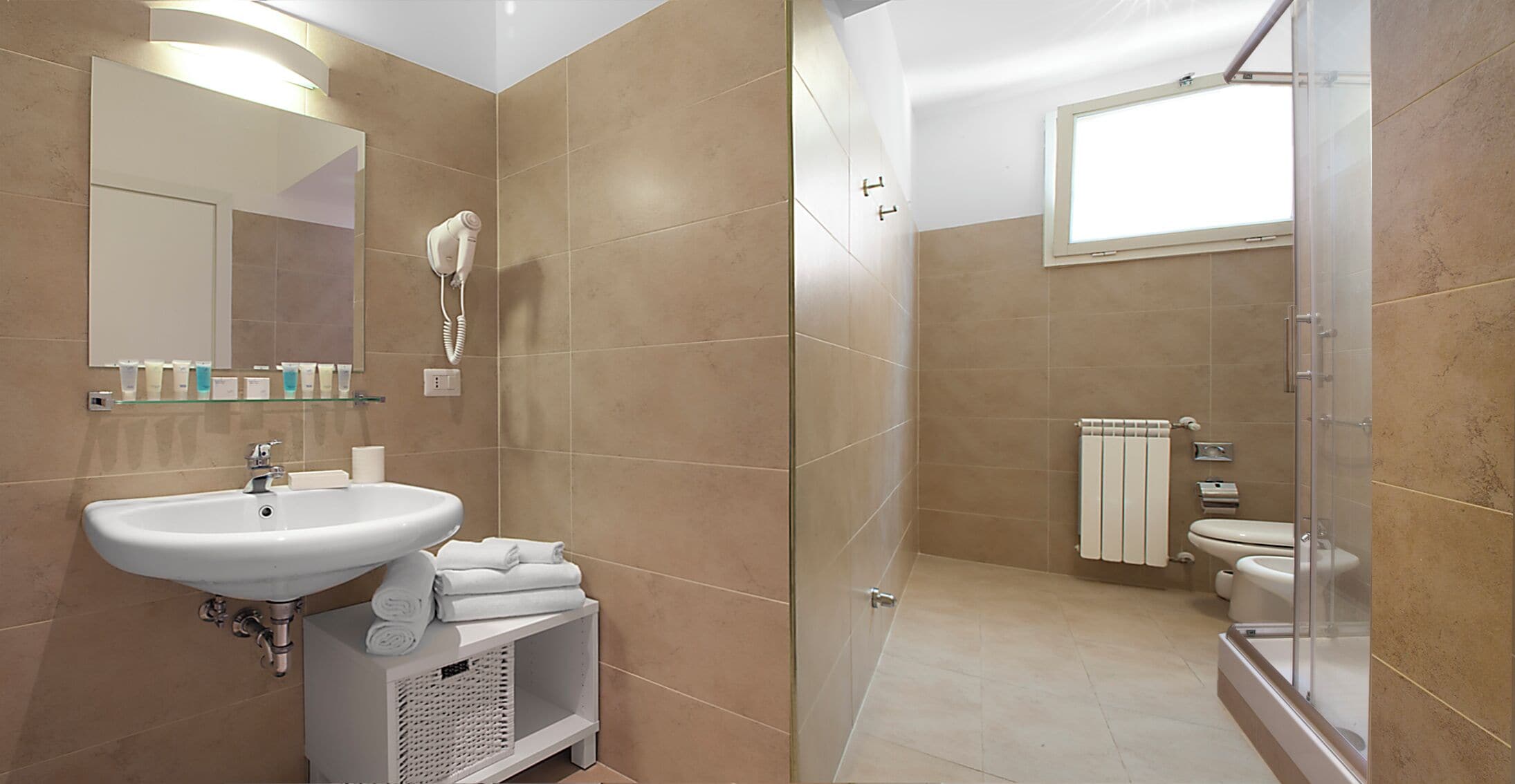 Une salle de bain moderne équipée d’un lavabo, d’un miroir, d’un sèche-cheveux et d’une douche à parois en verre.