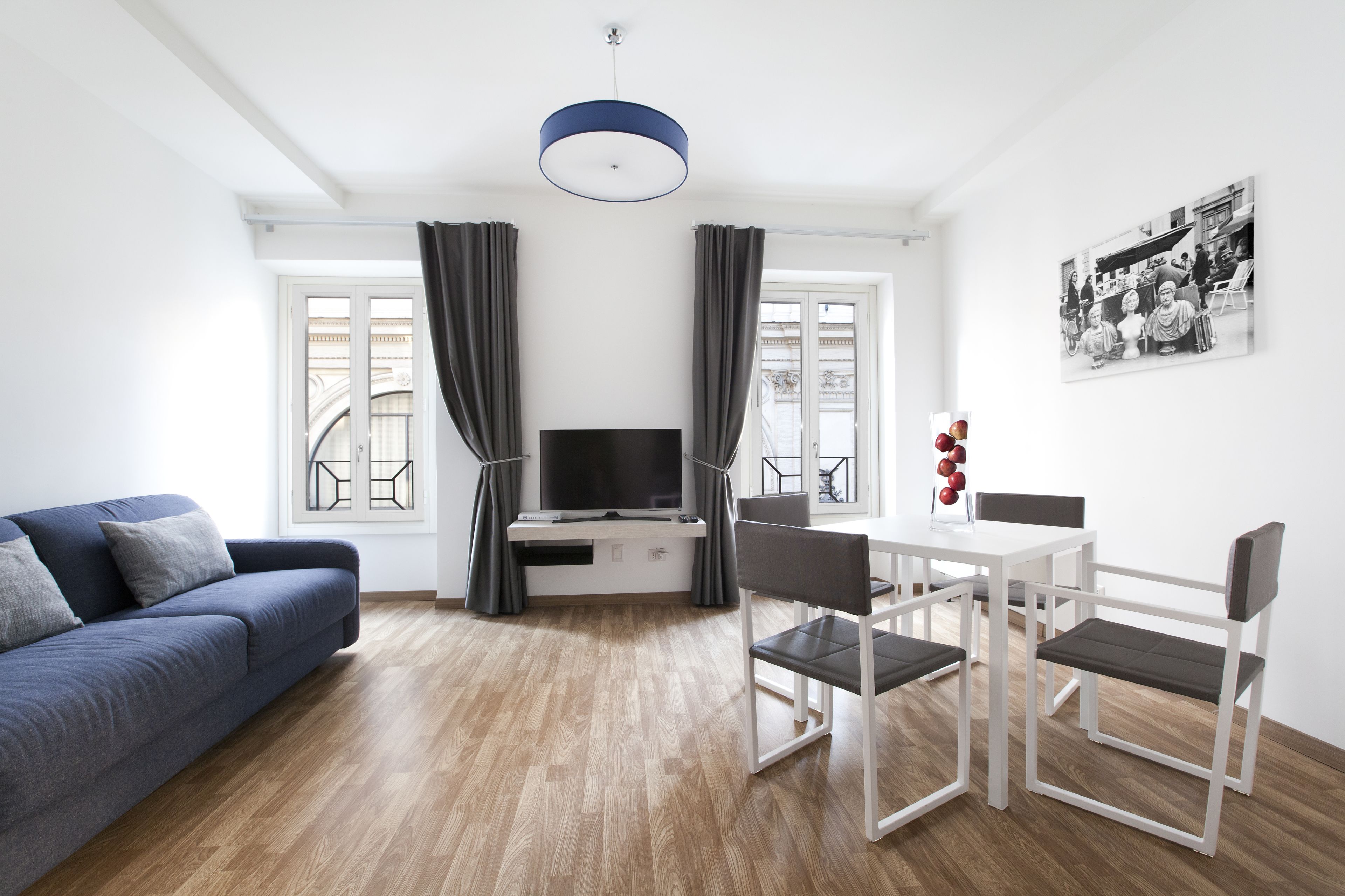 A modern living room with a sofa, TV, dining table, chairs, and curtains.