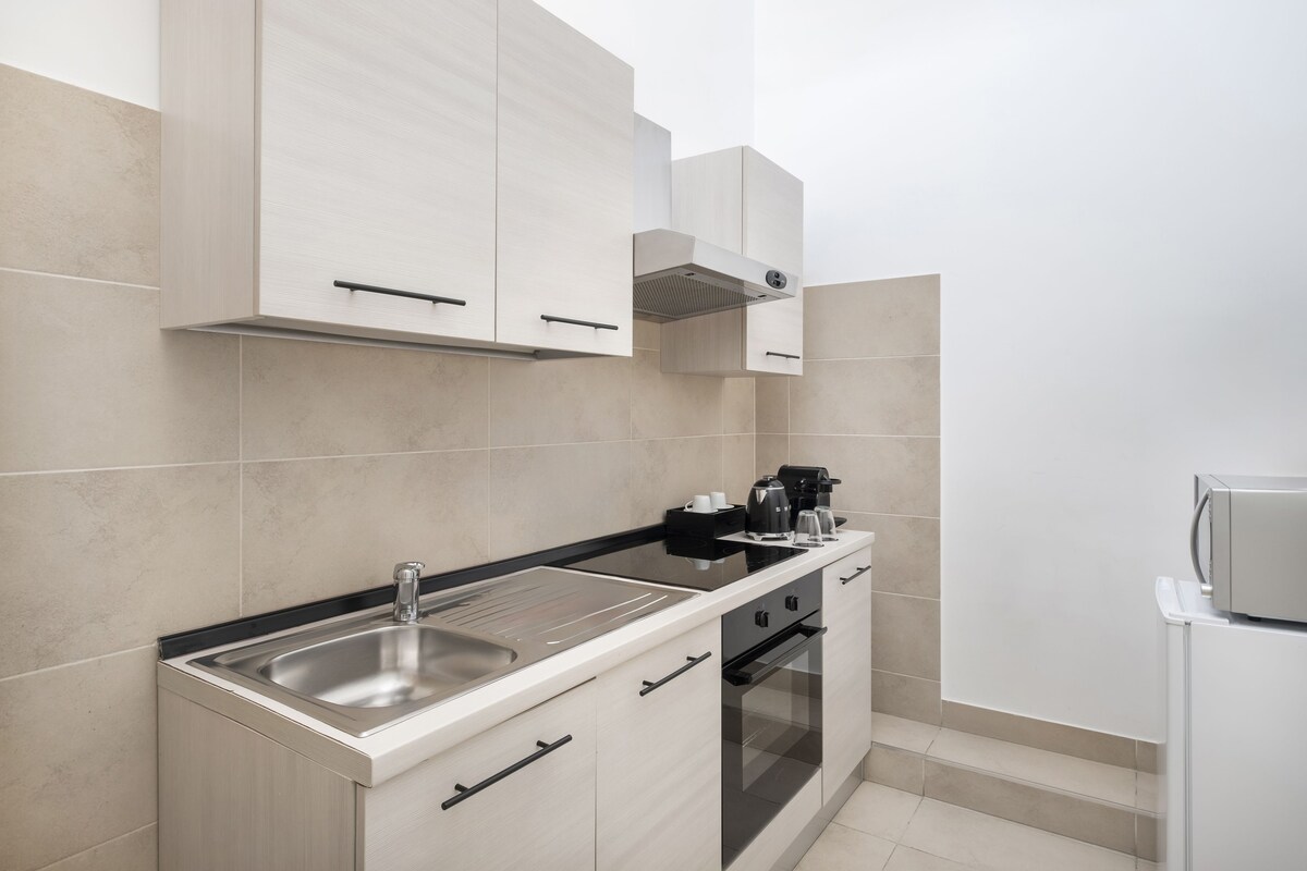 Uma cozinha moderna com pia de aço inoxidável, bancada preta e armários brancos.