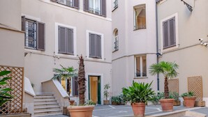 A narrow urban courtyard with terracotta planters, a palm tree, and a staircase leading to a building entrance. - Oriana Homèl Roma (Rome)