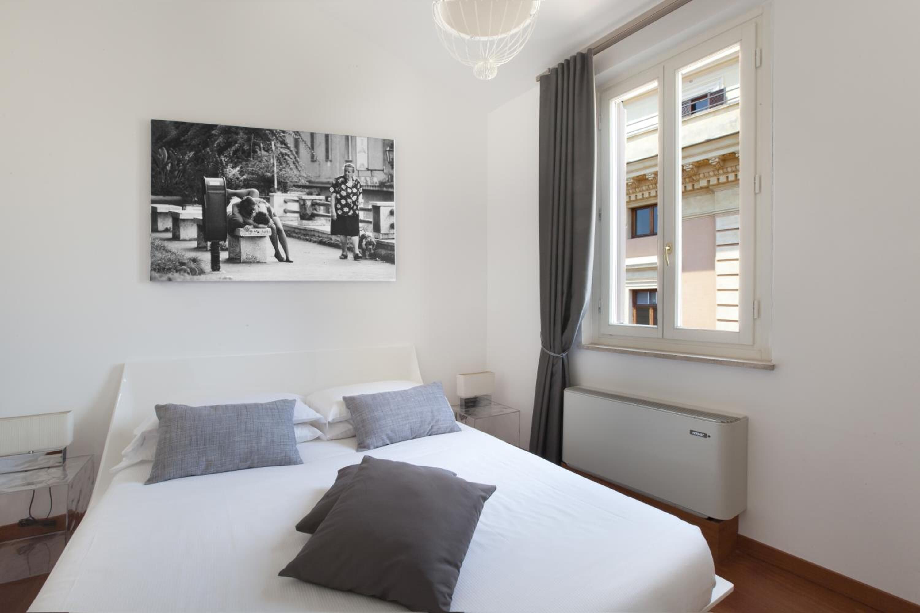 Ein Schlafzimmer mit Bett, Nachttisch, Lampe, Heizkörper und einem Fenster mit Vorhängen.
